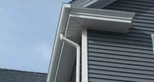 Gutters at the corner of a gray house, with blue sky in background.