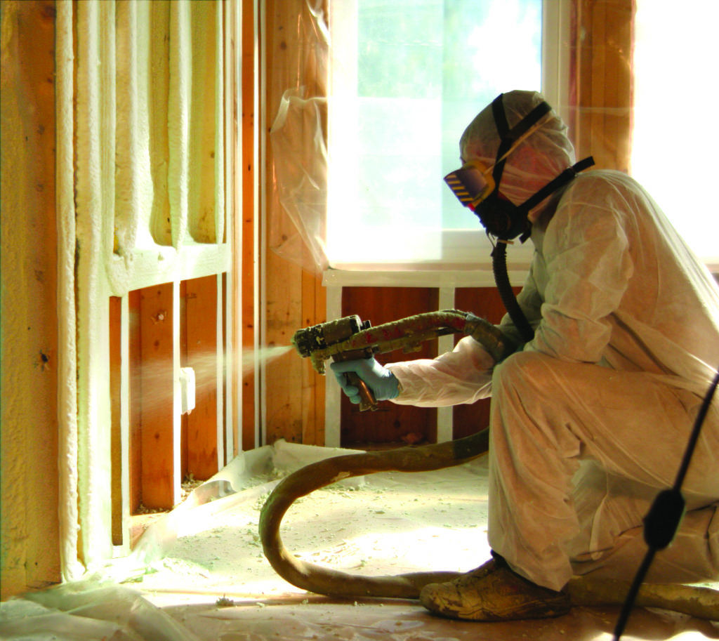 Spray foam insulation being applied to an unfinished wall by a technician in a hazmat suit.