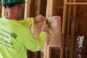 An Edwards/Mooney & Moses technician installing batt insulation