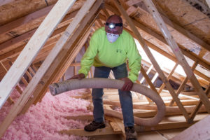 An Edwards, Mooney, and Moses technician adding loose-fill insulation to an attic