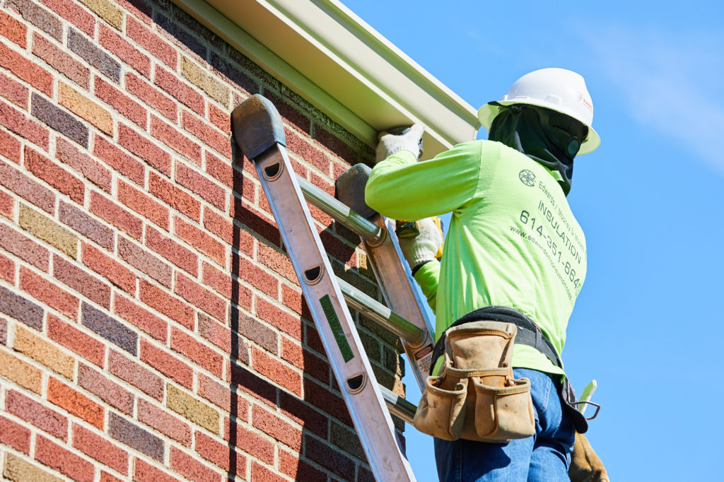 Commercial gutters being installed on brick building by technician on a ladder, wearing a hard hat.